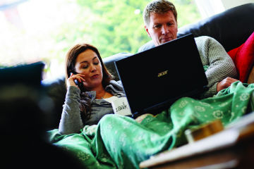 Couple sat on their sofa with laptop and phones